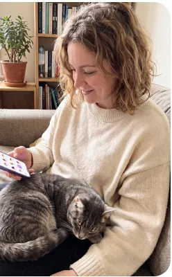 Lena reading a translation on her phone with a grey cat asleep in her lap