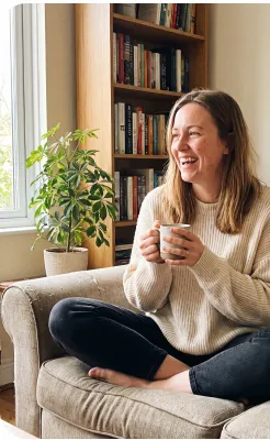 Lena laughing on the sofa with a mug of tea